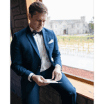 Groom in formal suit sitting by window checking phone at Castle Waterford wedding venue