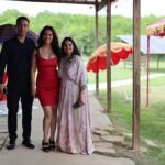 Three people walking together outdoors at an event venue with umbrellas and garden pathway