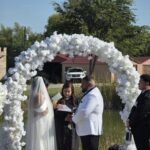 Outdoor wedding ceremony under white floral arch with bride and groom at Castle Waterford