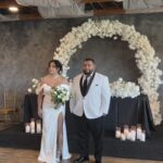 Bride and groom standing under white floral arch at Castle Waterford indoor wedding setup