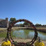 Circular floral wedding arch by lakeside at Castle Waterford with scenic outdoor setup