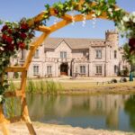Castle Waterford view through floral wedding arch by lakeside with scenic reflection