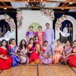 Large family group posing together in traditional Indian outfits at a wedding stage with floral decor