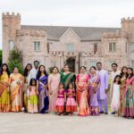 Large group of people in traditional Indian attire posing outside a grand building during a celebration