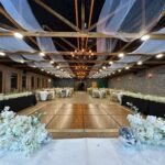 Elegant indoor wedding aisle with floral décor, draped ceiling, and stage setup at Castle Waterford