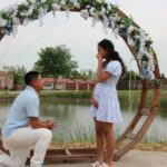 Man proposing to woman under circular floral arch by lake at Castle Waterford