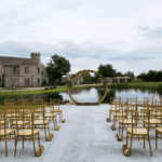 Outdoor wedding aisle with golden chairs and circular arch setup near lake at Castle Waterford