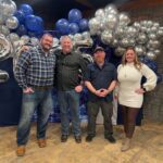 Group of people posing together in front of blue and silver balloon decoration at a celebration