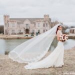 Bride with long flowing veil holding bouquet near lake at Castle Waterford wedding photoshoot