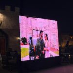 Large outdoor LED screen displaying a couple’s photo at an event venue at night.